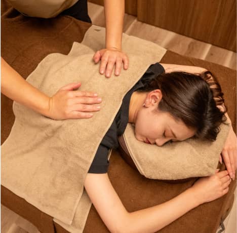 施術台でリラックスした表情を見せる女性に、セラピストが背中をケアしている様子