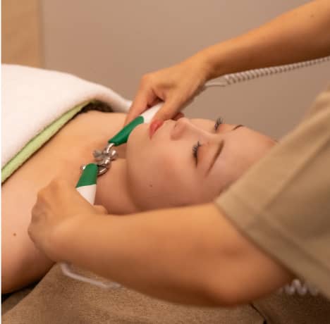 セラピストが緑と白のハンドルの器具を使ってフェイシャルトリートメントを施している女性